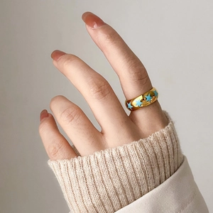 Close-up of golden wide ring with blue enamel stars worn on finger with a knit sweater