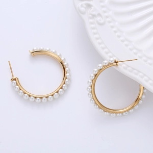 Detail of C-shaped gold hoop earrings with white pearls on a minimalist white ceramic background