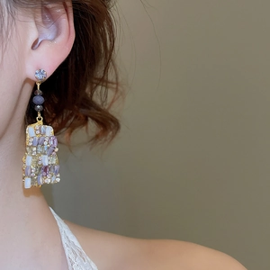 Dettaglio di orecchini pendenti dorati geometrici con cristalli viola su una modella