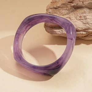 Detailed view of thick purple marbled resin bracelet leaning against a natural stone