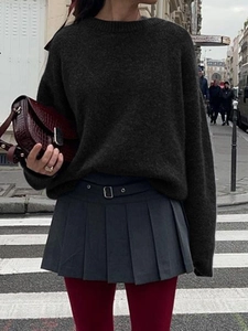 Close-up of a dark green knitted sweater styled with a grey pleated skirt and belt