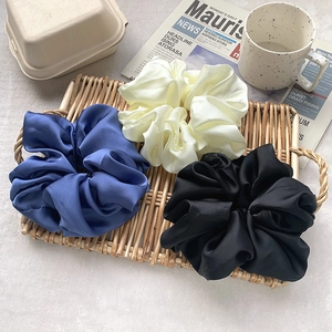 Close-up of three oversized satin scrunchies in navy, cream and black on a tray