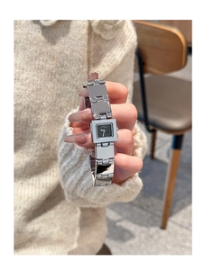 Détail d'une montre carrée argentée pour femme avec cadran noir portée sur un pull blanc