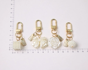 Detailed view of four golden pearl keychains with bow and rose pendants next to a ruler