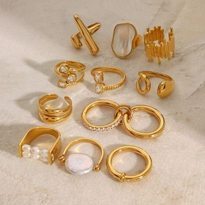 Golden stainless steel rings set featuring shell zircon and pearls on beige marble surface