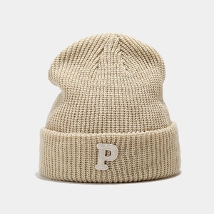 Detailed view of beige knit beanie with white fuzzy P letter patch and thick ribbed texture