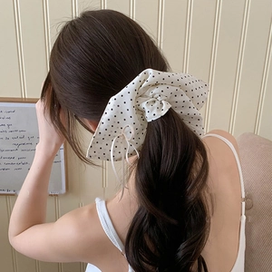 Detail of a large polka dot bow scrunchie on a ponytail from a back view perspective