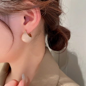 Close-up of minimalist cream bean geometric hoop earrings on a model's ear