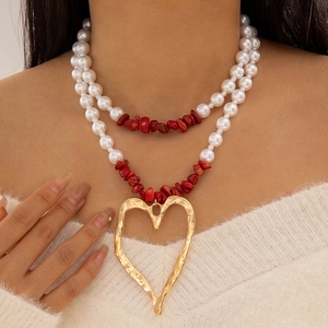 Detail of layered necklace featuring faux pearls, red stone beads, and a gold heart pendant