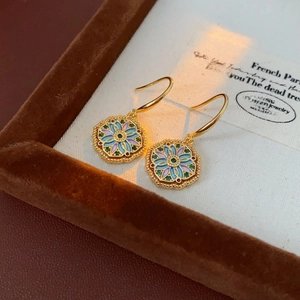Detailed macro view of vintage gold-plated floral earrings with green zircon in a box