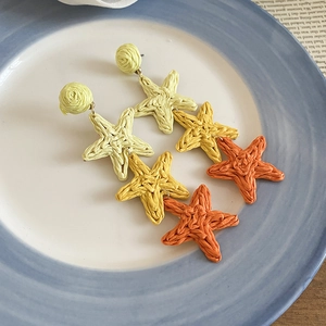 Detail of hand-woven raffia star tassel earrings in yellow and orange gradient tones