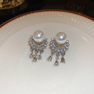 Close-up of silver tassel earrings with round pearls and sparkling pavé crystals on a plate