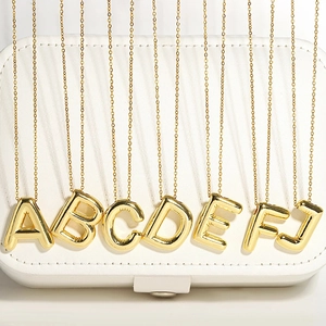 Dettaglio in primo piano della collana con ciondolo a lettere dorate, catena fine, rame.