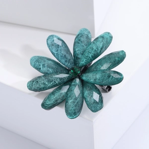 Detailed close-up of teal acrylic flower brooch with green rhinestone on white podium
