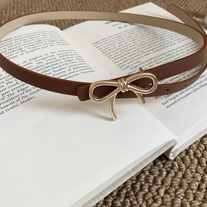 Detailed shot of dark brown leather belt featuring a golden bow-shaped metal buckle on a book