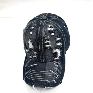 Detailed view of distressed dark denim baseball cap with heavy fraying and white stitching