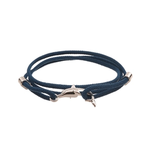 Detail of a dark blue braided cord bracelet featuring a polished dolphin-shaped metal clasp