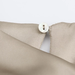 Macro-opname van witte schelpen knoop op de kraag van beige zijden satijnen jurk