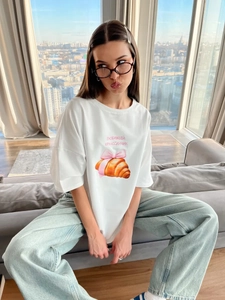 Λεπτομέρεια λευκού βαμβακερού T-shirt με τύπωμα κρουασάν, ροζ φιόγκο και ρωσικό κείμενο