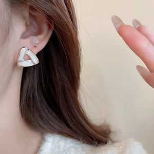 Close-up of geometric triangle earring in white enamel and gold metal on a model's ear