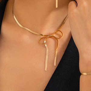 Detail einer goldenen Schlangenkette als 3D-Schleife am Schlüsselbein einer Frau