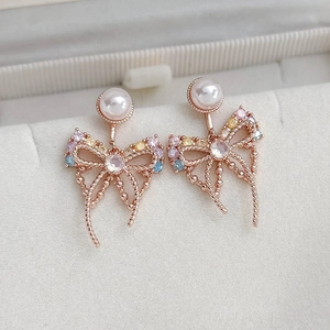 Macro shot of rose gold bow earrings with colorful zircons and a white pearl detail