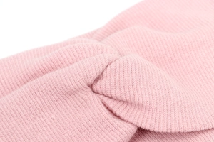 Close-up of pink knitted baby headband showing cross knot design and ribbed texture