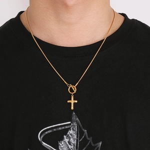 Detail of gold cross pendant necklace with snake chain and toggle clasp on a model
