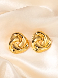 Detail of gold twisted triangle knot earrings on premium champagne satin fabric