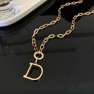 Macro detail of rose gold necklace featuring a black enamel letter D pendant with diamonds