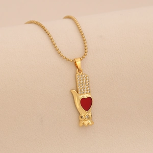 Macro detail of gold beaded necklace with a crystal-encrusted hand and red heart pendant