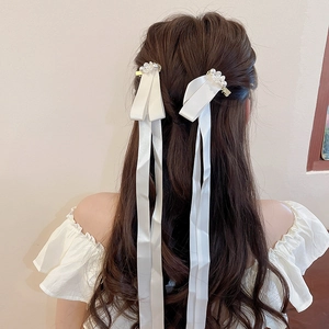 Detail of elegant white satin bow hair clip with pearls and long streamers on hair