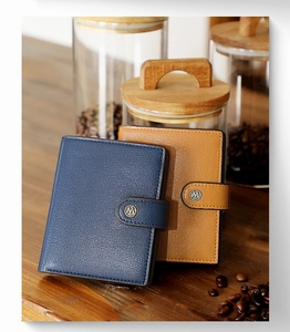 Detail of dark blue leather wallet with metal buckle and M logo on wooden table