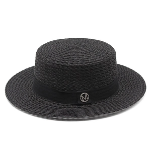 Close-up of a black straw hat featuring a rhinestone-embellished metal M logo and ribbon