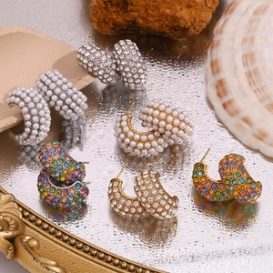 Macro shot of 18K gold C-shaped earrings with pearls and colorful crystals on reflective base