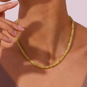 Close-up of beaded necklace featuring pale yellow cylindrical stones and gold metal beads