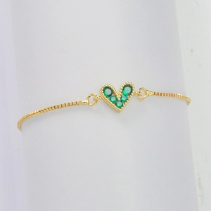 Adjustable gold heart bracelet featuring five green cubic zirconia stones on white background