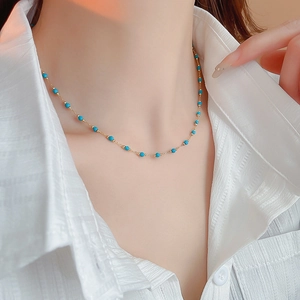 Detail of bohemian gold-plated necklace featuring blue beads on model's neck