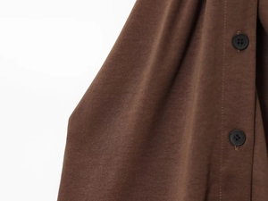 Close-up of brown textured fabric with black four-hole buttons on high-waist pleated pants