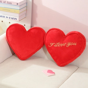 Pair of red plush heart pillows with golden I Love You embroidery on white sofa
