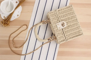 Detail of cream woven box bag with golden metal lock and chain strap on table
