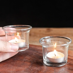 Minimalist clear glass tea light candle holder with a warm glowing flame on a wood table