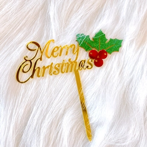 Detail of golden acrylic Merry Christmas cake topper with green holly leaves and red berries