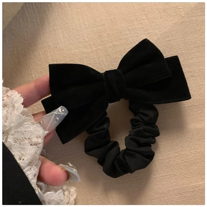 Close-up of a large black velvet bow scrunchie held by a hand on a soft beige fabric