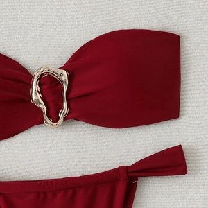 Detail of burgundy bikini top with a gold metallic buckle on a white textured surface