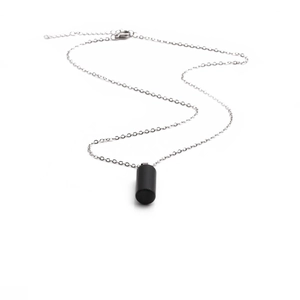 Detail view of a black cylindrical stone pendant with a silver lobster clasp chain