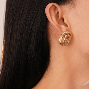 Close-up of golden geometric earrings with hammered texture and spiral oval design