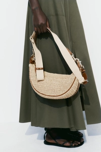 Detail of beige woven crossbody bag with brown leather trim and canvas strap on model