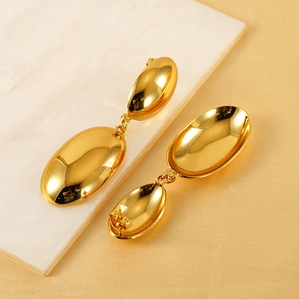 Macro detail of gold oval double-link drop earrings on a marble and fabric surface