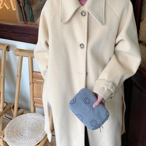 Detail of grey corduroy cosmetic bag with smiley face held against a white wool coat